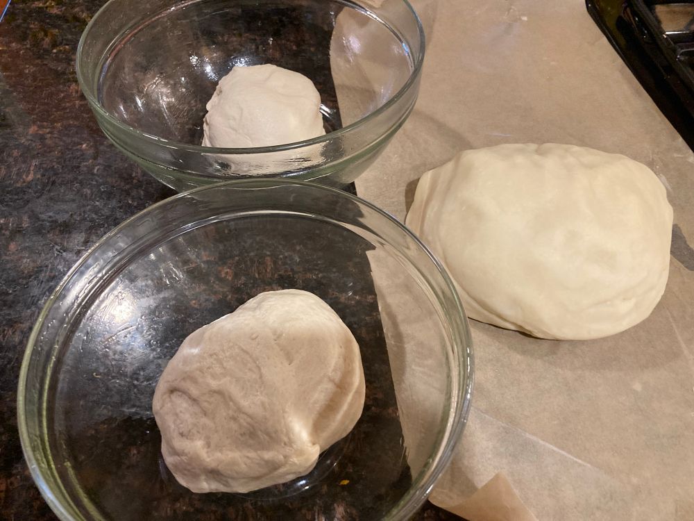 Two bowls with white dough next to a big blob of dough on wax paper. 