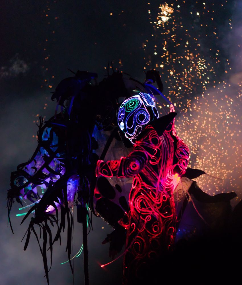 A nighttime scene featuring a horse figure and a person dressed in glowing neon lights. In the background there are bright sparks.