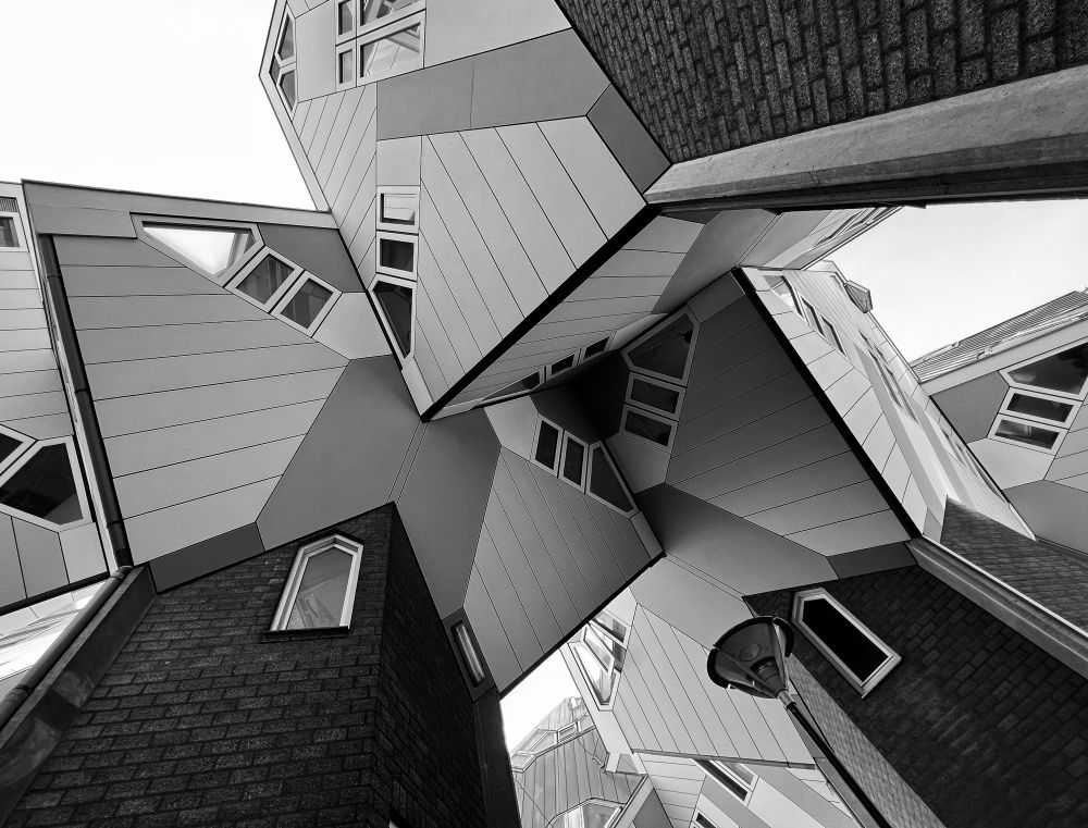 A black and white photograph of a building with geometric shapes and irregular angles, viewed from a low perspective.