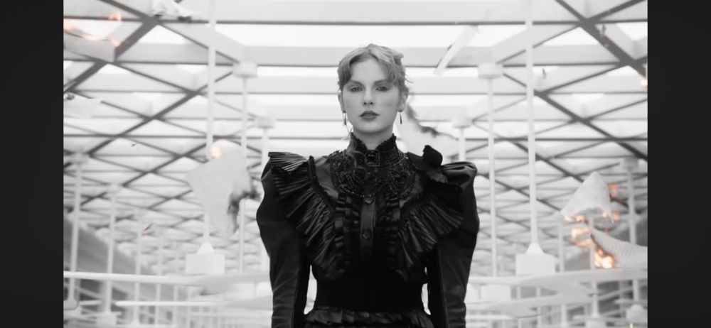 Taylor, standing and staring directly at the camera as flaming papers fall into ash around her 