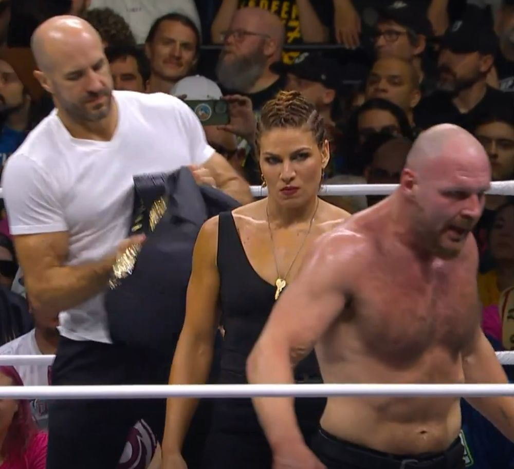 [Image: Moxley at Wrestledream 2024 after shoving the belt at Claudio, who is stuffing it in a nondescript black nylon duffel bag. Commentary asks 'what's the significance of putting the AEW Championship in a bag?' Marina is seen next to them clearly already wearing a key around her neck.]