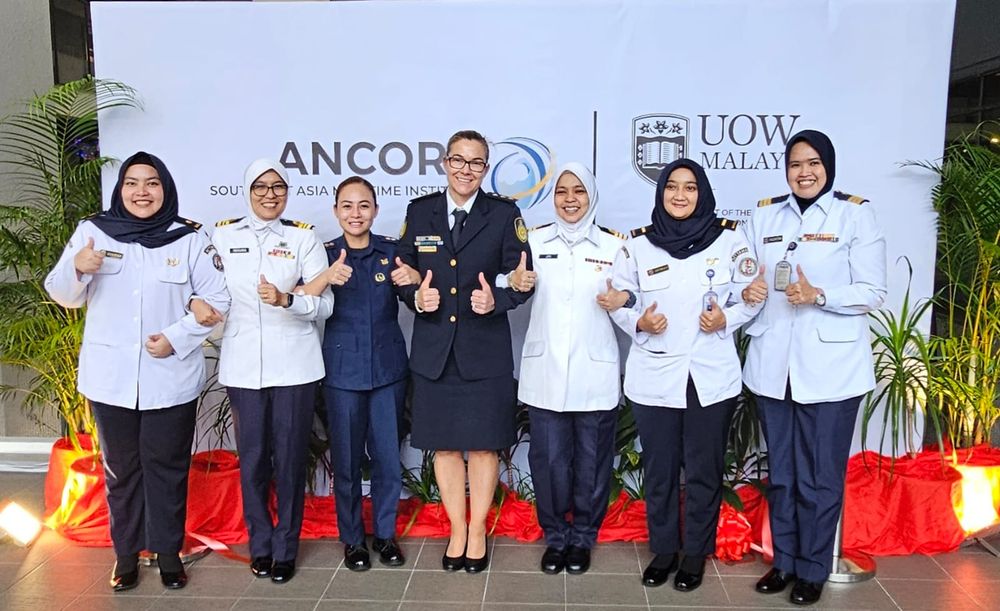 A group of seven uniformed officers from coastguards and navies of different countries, posing together in front of the UOW Malaysia sign