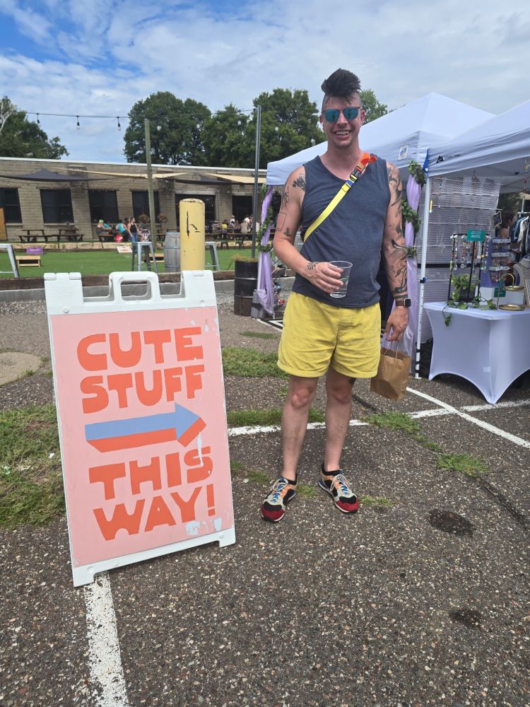 a sign says "Cute Stuff This Way" with a big painted arrow pointing to the right of the image, where a tall goofy dude stands with a shit eating grin on their face