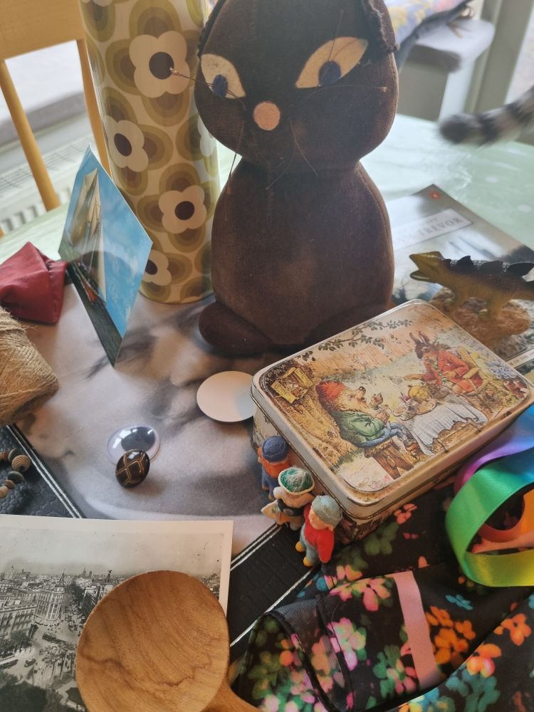Collection of objects including a velvet toy cat, a tin featuring a hedgehog and hare sitting down to tea, a button, a plastic dinosaur, tiny plastic people, and more...