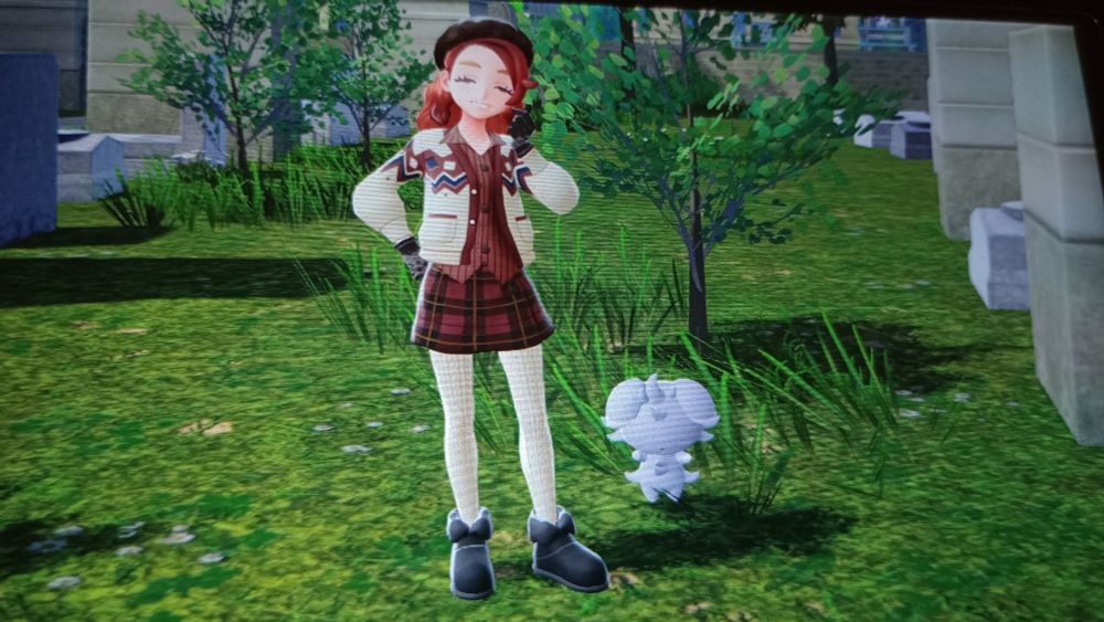 a pic of trainer Io Lynn and her Espurr. outfit is a white, blue and brown patterned cardigan over a brown button up shirt, red and black plaid skirt, white knit leggings and black plush boots