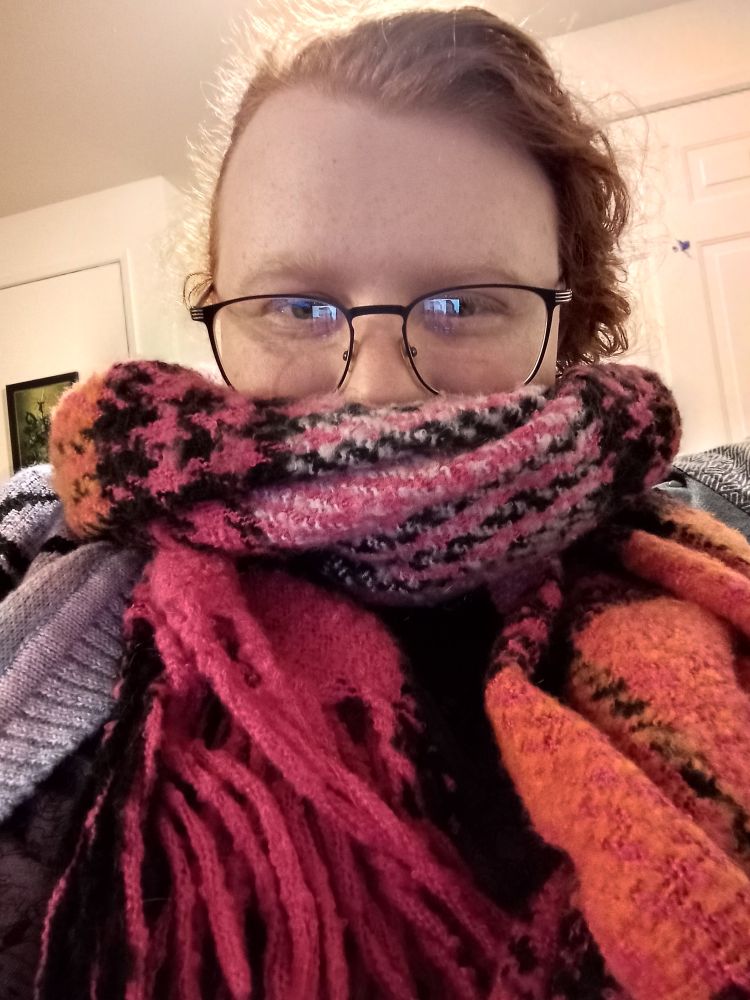 a picture of Io wearing a really big scarf (it's lesbian flag colors too!)