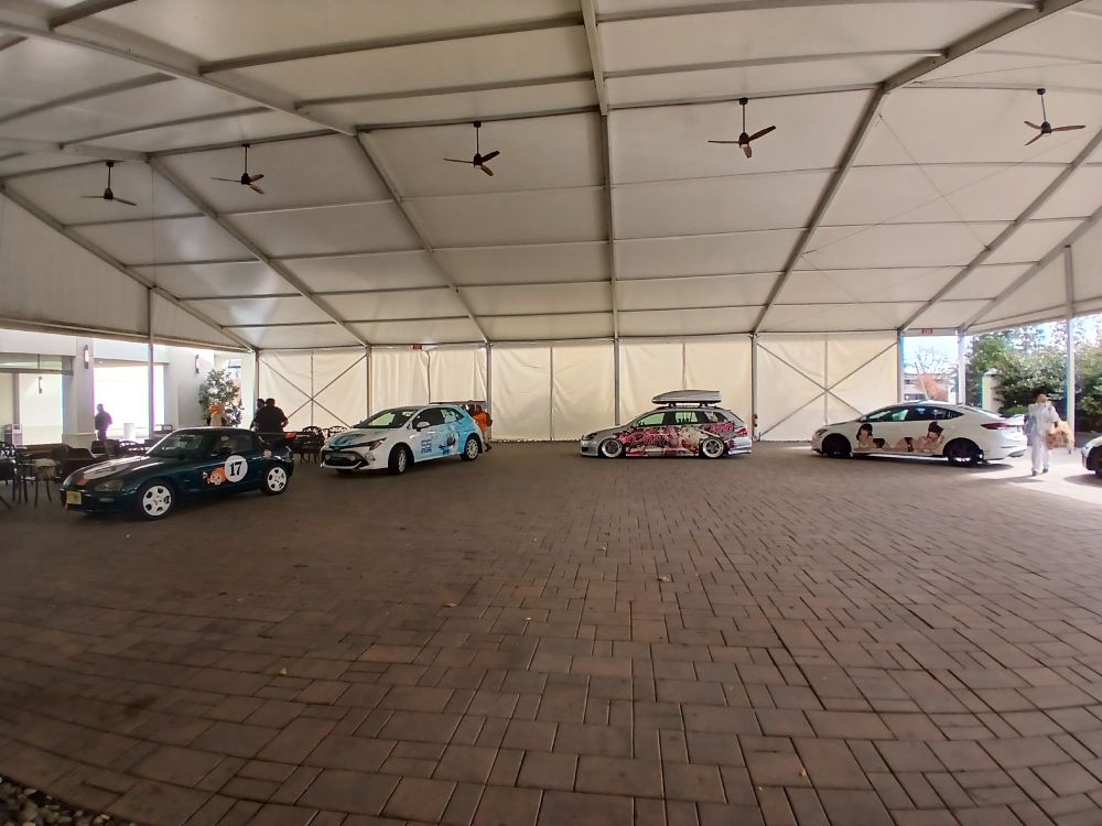 Japanese cars being displayed under a permanent tent partially shielded from the elements. 