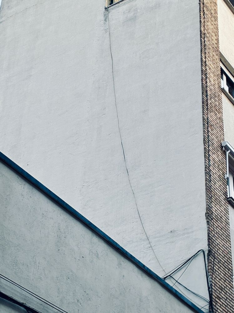Pared lateral blanca de una casa de viviendas atravesada por un cable negro de arriba abajo, haciendo una curva diagonal.