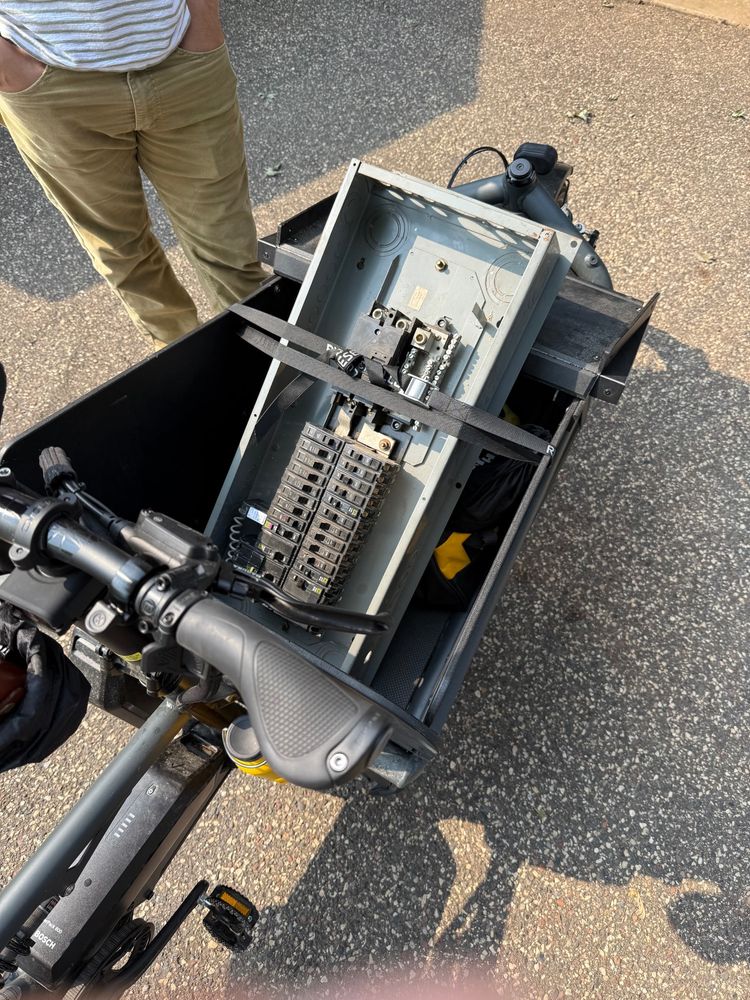An electrical panel strapped down in the cargo compartment of a front loading cargo bike