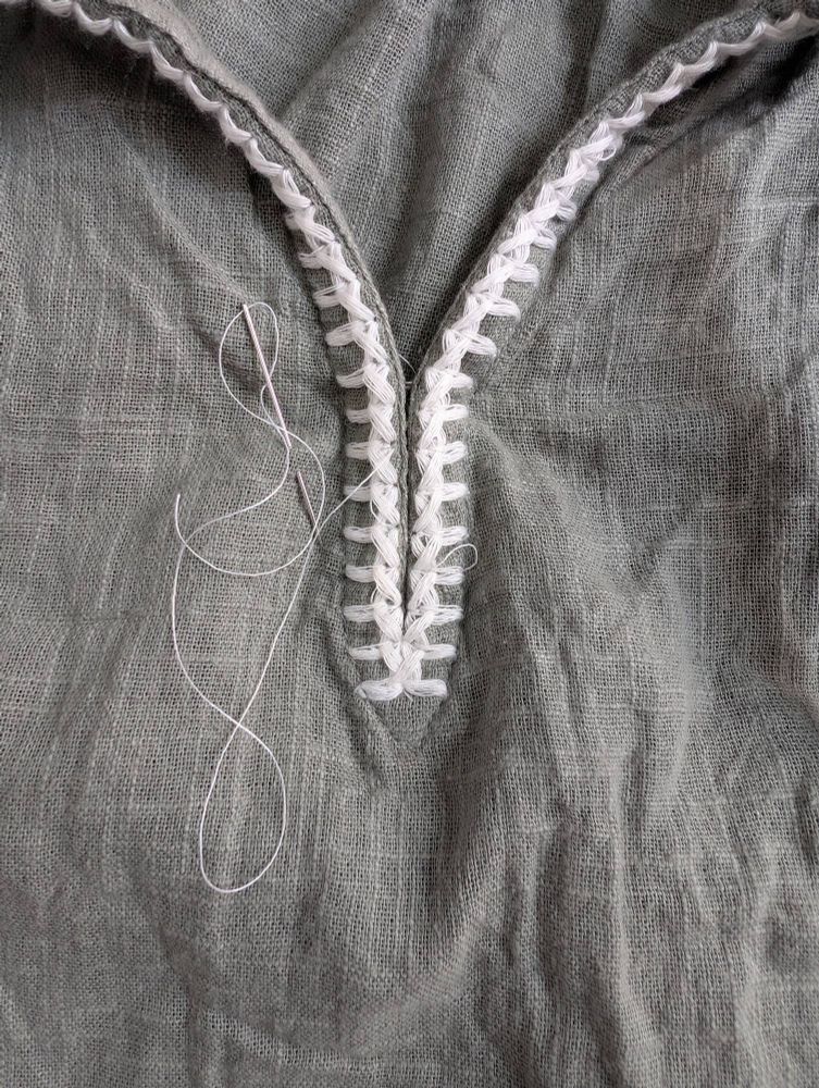 A V neck embroidered desaturated green top with white embroidery. It has been sewn so the two sides butt up against each other. The sewing needle and white thread is visible. I thought this join done in herringbone stitch was too weak to stand on its own. 