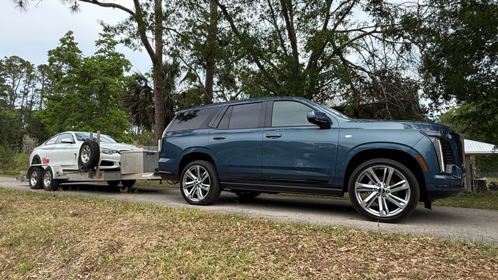 A 2025 Cadillac Escalade tows a double-axle aluminum trailer carrying a BMW 435i track car.