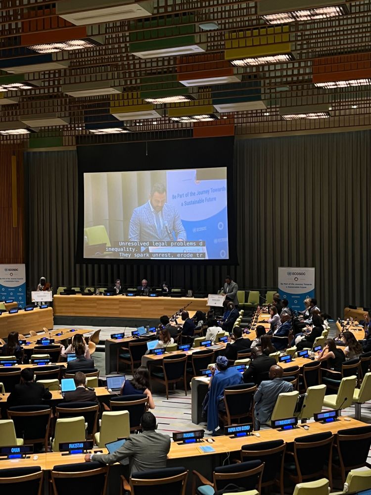 Wide-angle shot of the ECOSOC chamber, with participants looking at a screen of the speaker.
