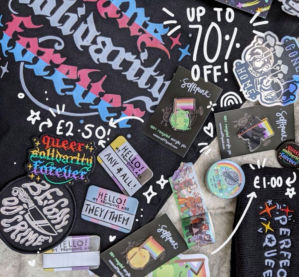 a flat lay of various Sofftpunk products including pride pins, pronoun badges, embroidered patches, pride parade washi tape, a trans Solidarity forever Tote bag and a perfectly queer beanie