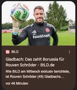 Ein Mann in Trainingskleidung mit der Aufschrift „toolcraft“ steht auf einem Fußballplatz und hält mit der rechten Hand einen Fußball in die Kamera. Im Hintergrund sind Rasen, Bäume und ein Tor zu sehen.