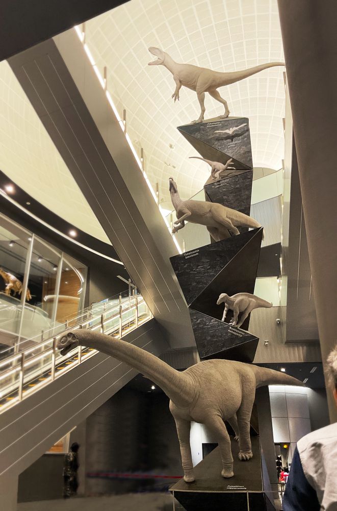 커다란 공룡 모형이 4층을 관통하는 빈공간에 놓여있다. 까만색의 기하학적인 기둥에 위에서부터 하나씩, 가장 위는 공룡, 그 아래는 새, 다시 그 아래로 공룡들. 총 여섯이 있음. 