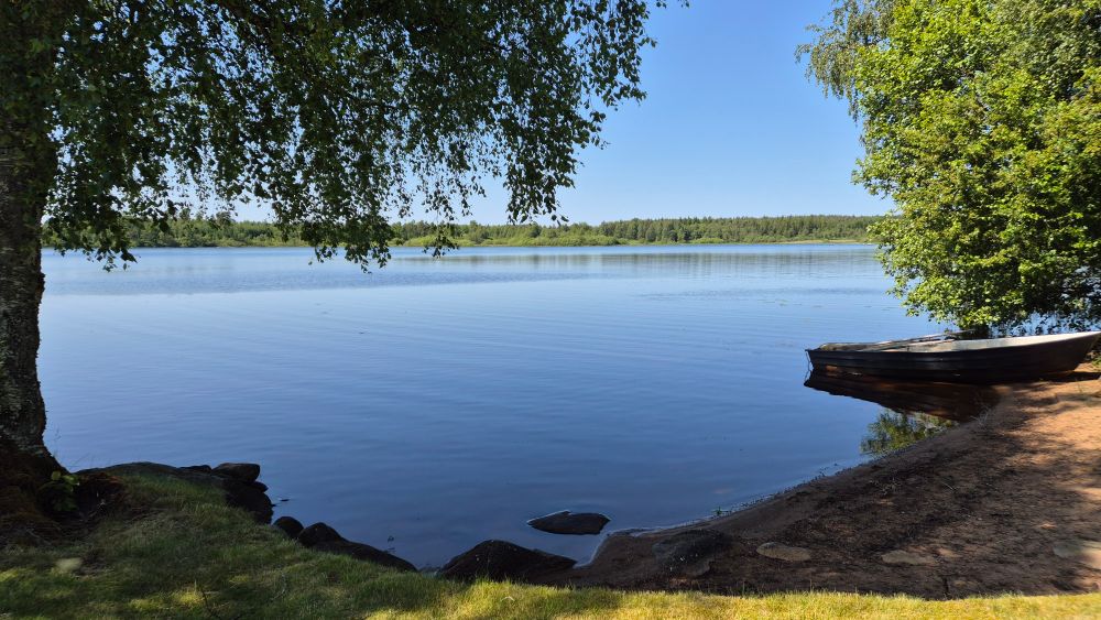 Liten sandstrand vid en sjö. Blå sommarhimmel.