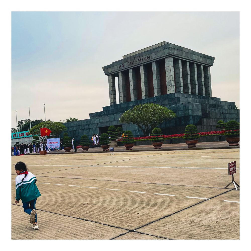 A girl runs across a line a sign tells her not to in front of the Ho Chi Minh mausoleum.