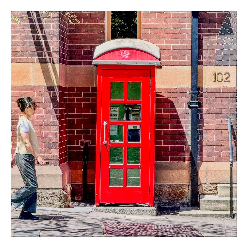 A traditional red telephone kiosk set against a red-brick wall. 