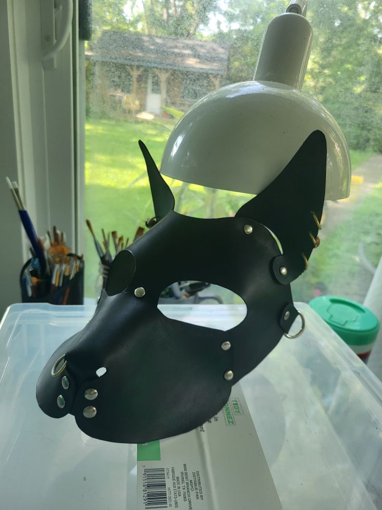 A dark green leather dog mask with gold hoop piercings.