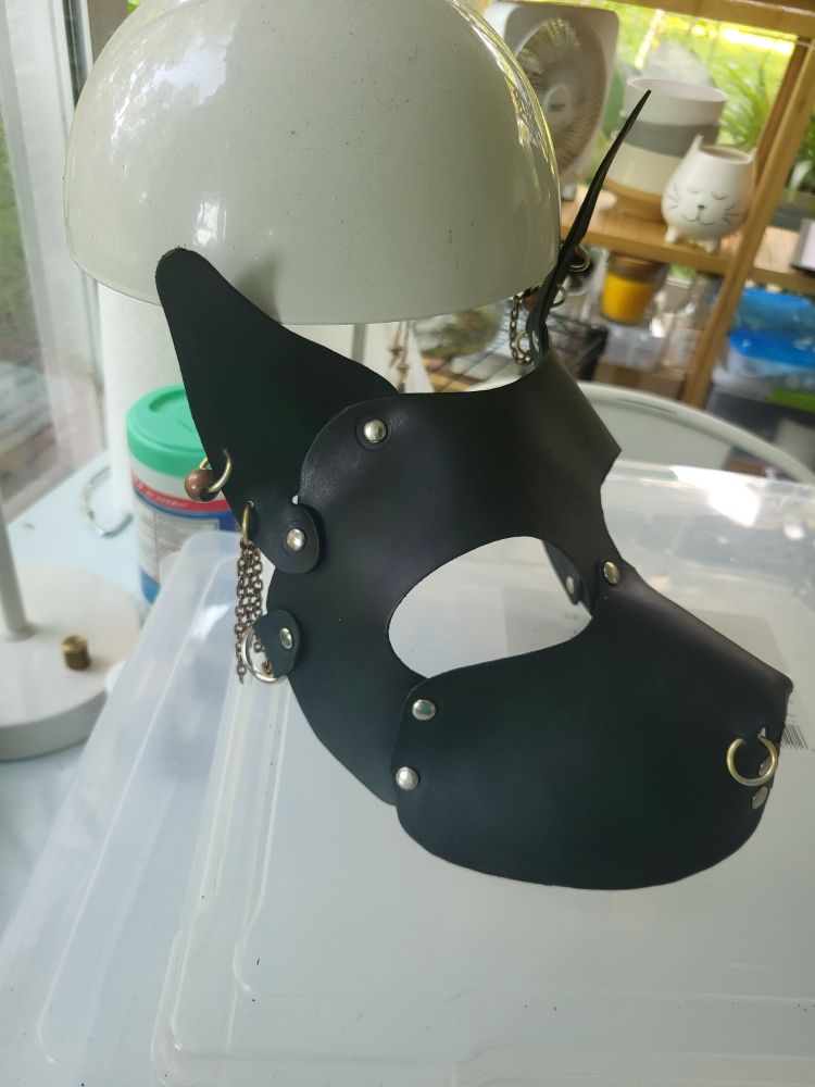 A dark green leather dog mask with gold hoop piercings.