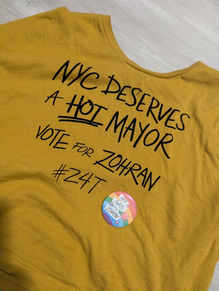 A yellow T-shirt that reads "NYC deserves a HOT mayor" "Vote for Zohran" "#Z4T" and a sparkly rainbow button which reads "Hot gays for Zohran"