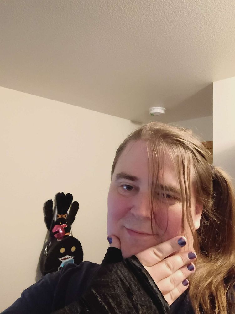 a picture of IRL Sylari, with a side tail and one hand under her chin, showing off her arm sleeve and her spriggans in the background. 

6 months on HRT