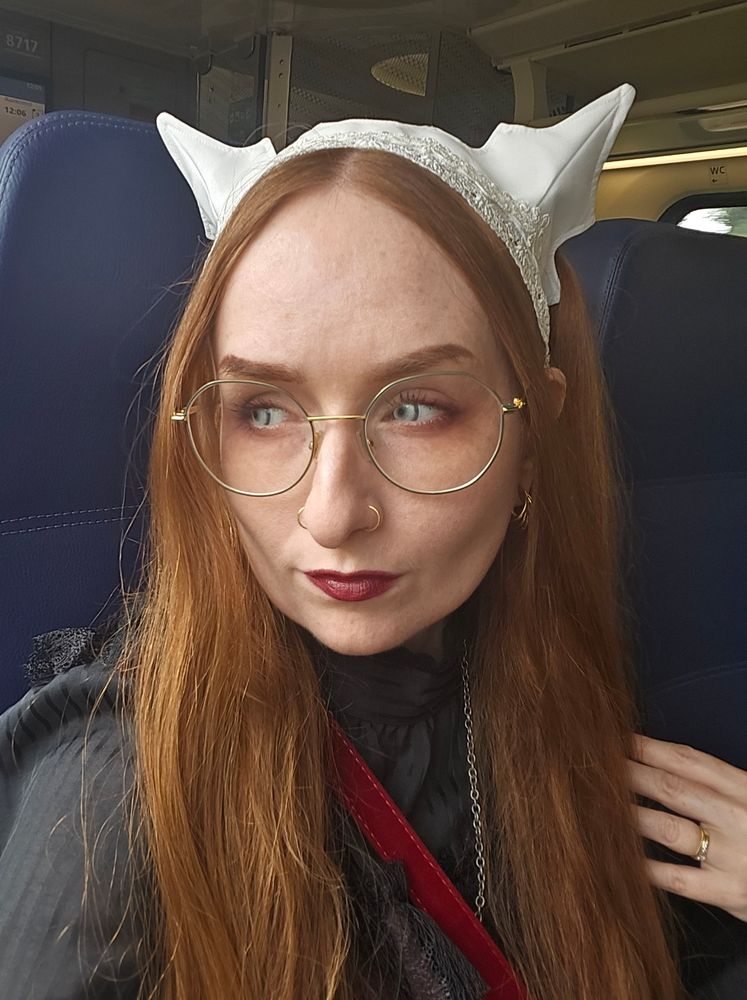 Selfie on the train. Wearing Antique BeasT bat/cat headdress in white and white contacts. Long red hair is worn in 2 long pigtails. Soft smokey red eyeshadow look pairwd with wine red lipstick.