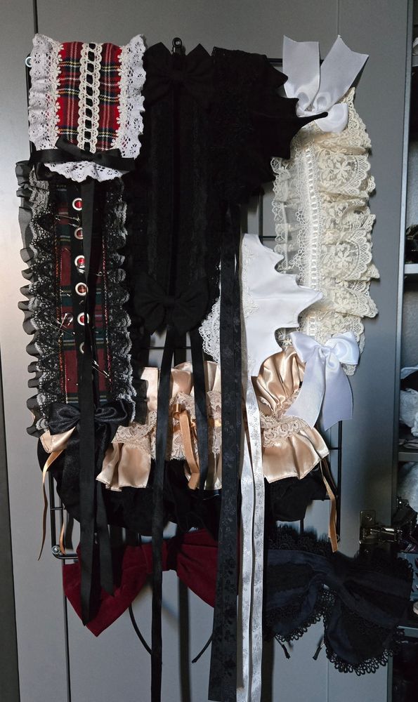 Photo of a closet door with a black grid wire wall panel mounted onto it. The panel hangs full with lolita headdresses and two headbows of various colours.