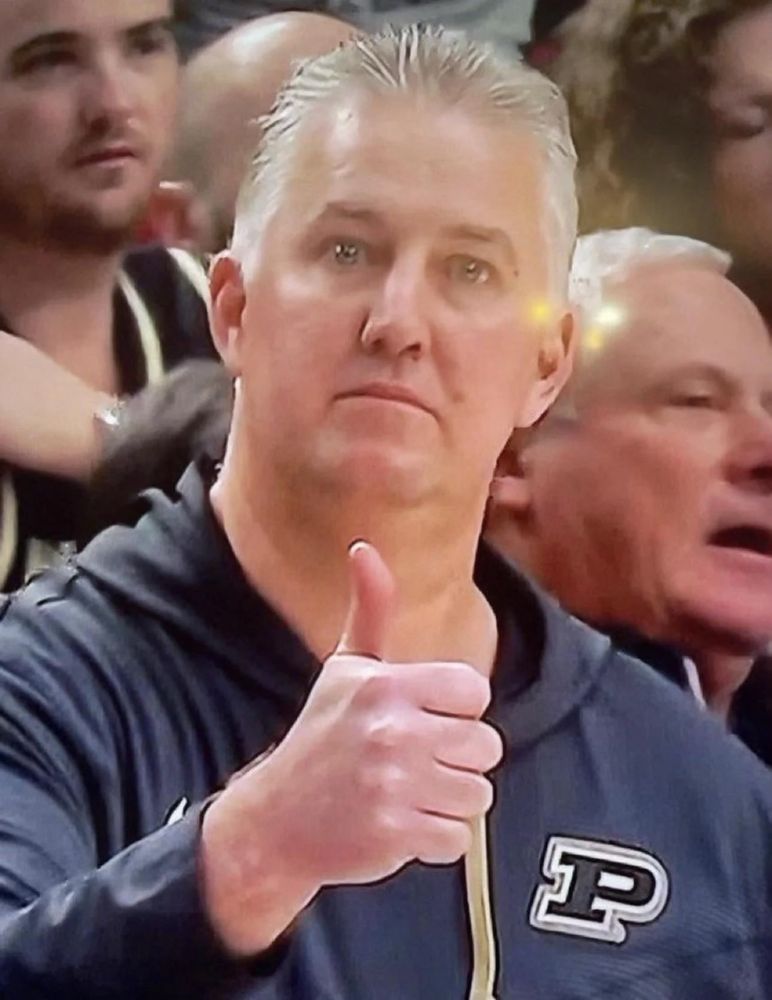 Matt Painter, coach of the Purdue Boilermakers Men’s Basketball team, gives an expressionless thumbs up while staring directly at the person taking the picture.
