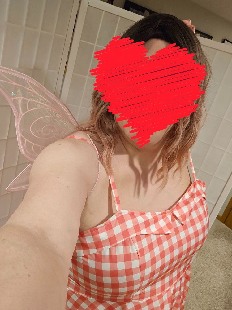 Maia, in a pink checkered dress, with pink hair bow, and pink fairy wings. her face is covered with a heart emoji.