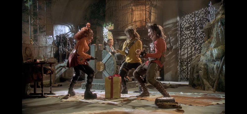 Burly, Blabberwort, and Bluebell excited about the new gift, shouting “Leather!” around a boxed gift. A bewildered Virginia stares at them from the background.