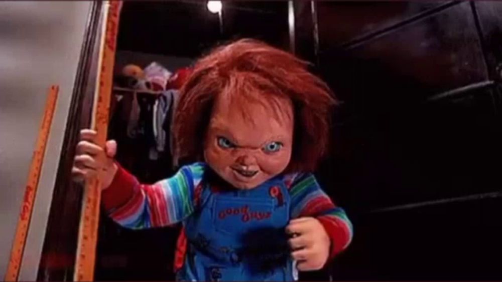 a chucky doll is standing in a doorway holding a stick .