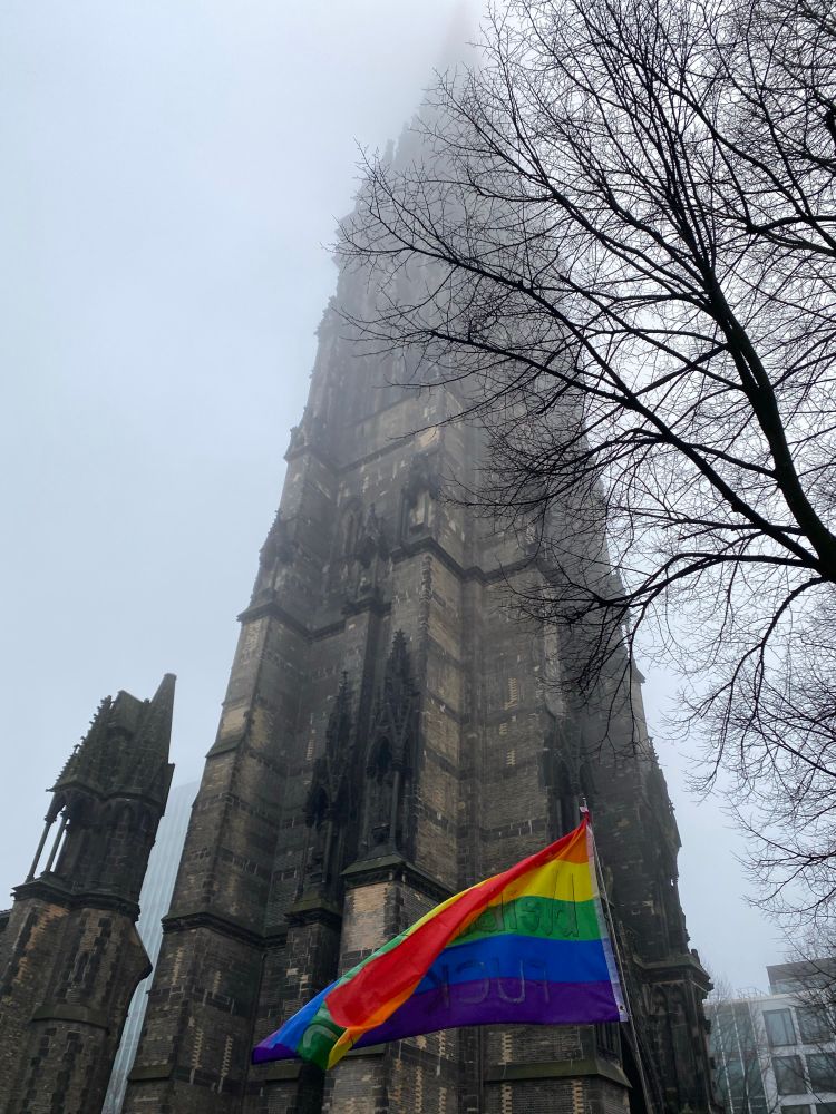 Der Turm der Hamburger Nikolaikirchenruine im Nebel, davor eine Regenbogenflagge. 