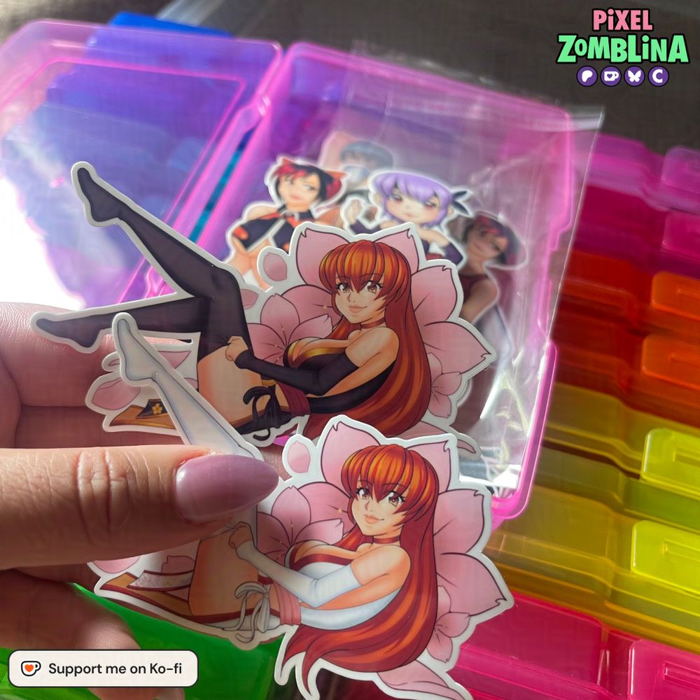 Two stickers of Kasumi from Dead or Alive. They are the same pose with her pulling down her stocking as she is laying down, but back up a bit. She is looking towards the viewer and has cherry blossoms behind her. You can see my Chibi Ayane, and Mila stickers.