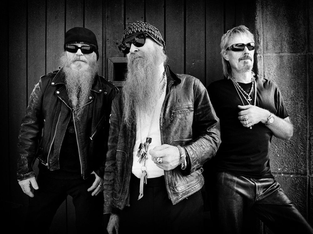 Black and white photo of the band ZZtop.  Three men, two with very long beards all wearing sunglasses.  
