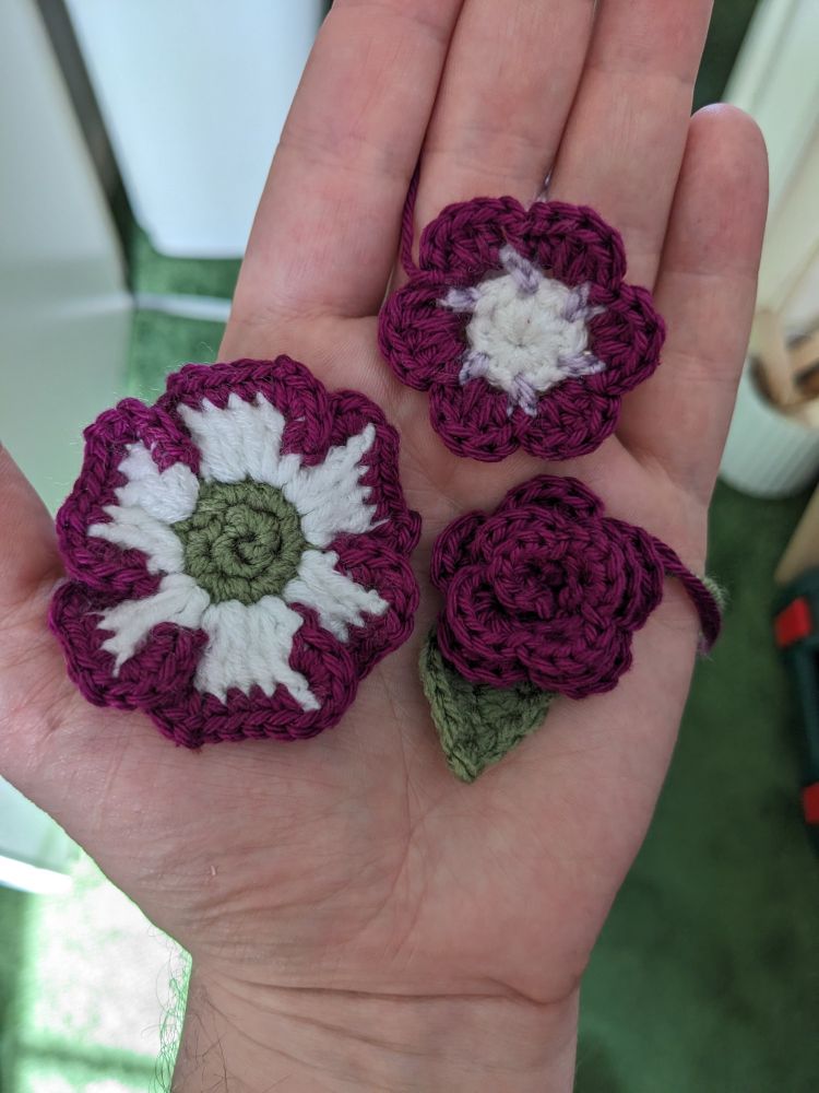 Three crochet flowers, made from white, purple and green yarn
