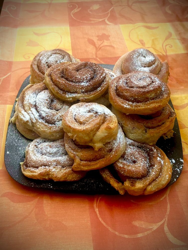 Un plato con varios rollitos de canela espolvoreados de azúcar sobre un mantel naranja y amarillo.