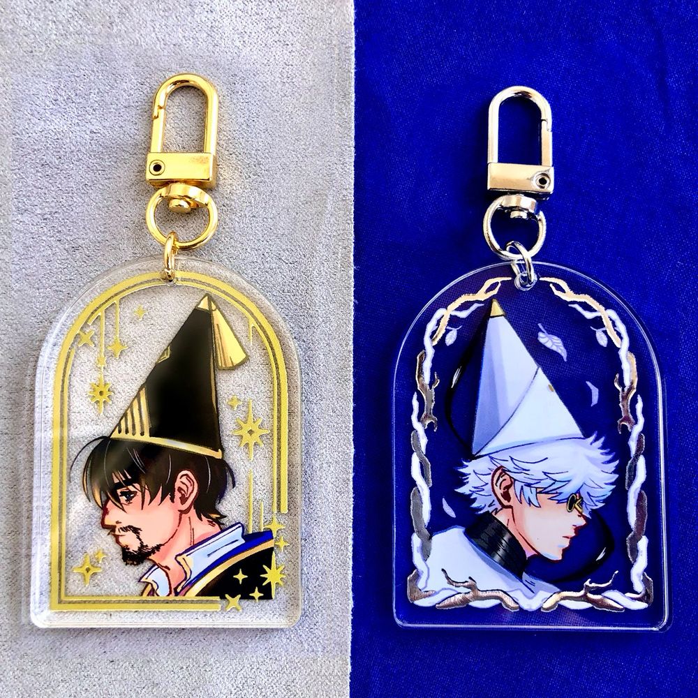 Acrylic charms with silver or gold foil featuring fan art depictions of Olly and Qifrey from WHA