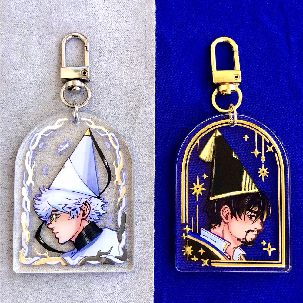 Acrylic charms with silver or gold foil featuring fan art depictions of Olly and Qifrey from WHA