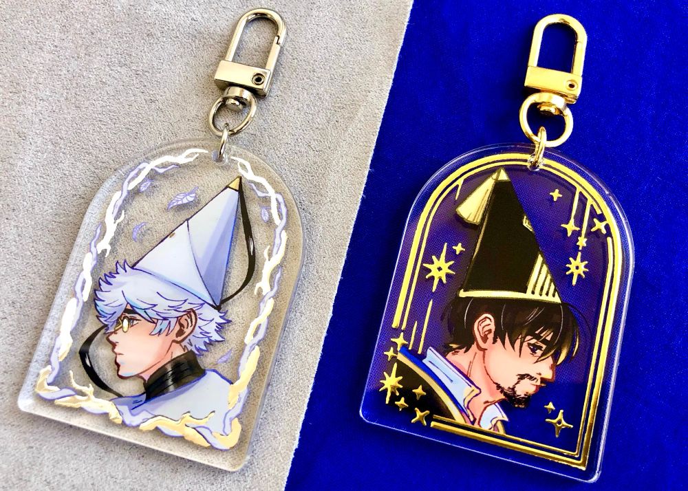 Acrylic charms with silver or gold foil featuring fan art depictions of Olly and Qifrey from WHA