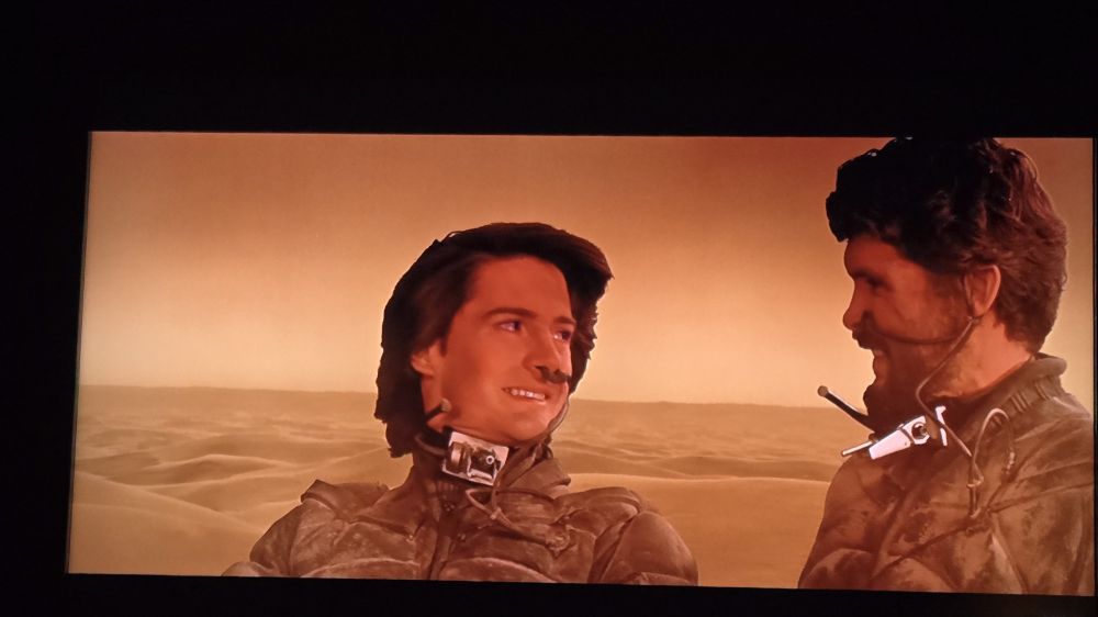 Still image from David Lynch's Dune-- Paul and Stilgar look at each other atop a sandworm.