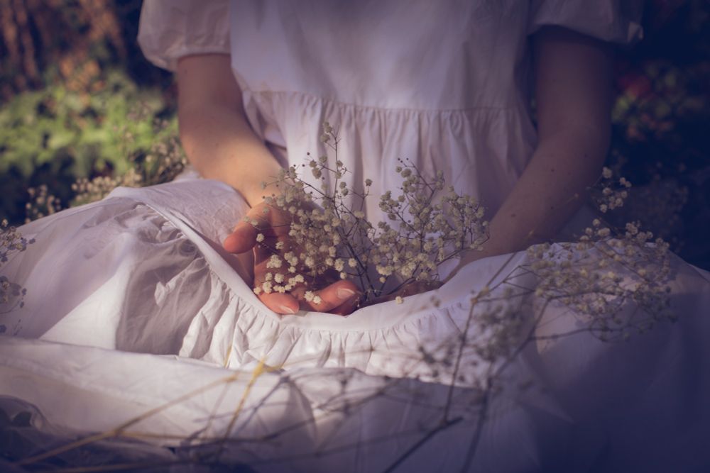 Ausschnitt einer sitzenden Frau in weißem Kleid mit Schleierkraut auf dem Schoß