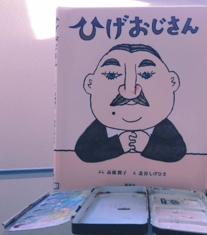 立てられた絵本の表紙（ひげおじさん）が、綺麗になった金属パレットを見つめているかのような写真。向かって左のパレットは掃除前。