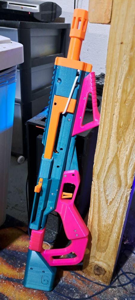 A mostly green 3d printed dart gun with pink accents and orange mechanisms.