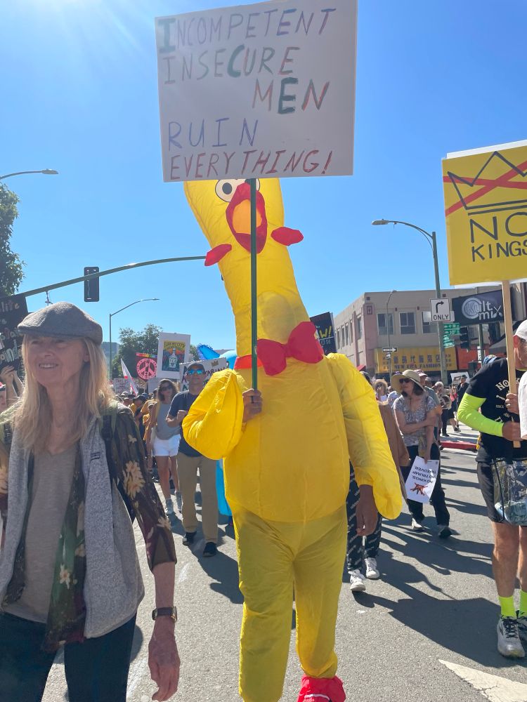 An inflatable chicken holding a sign saying “Incompetent insecure men ruin everything!