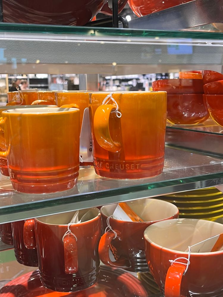 Two orange and red le cruset cups on display in a store