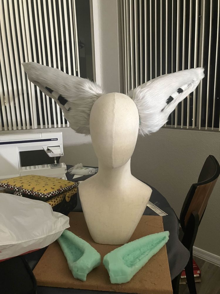 two large gray ears pinned to a mannequin bust, with the insides of them having black and white stripes. a smaller unfinished pair of ears sits at the base of the mannequin