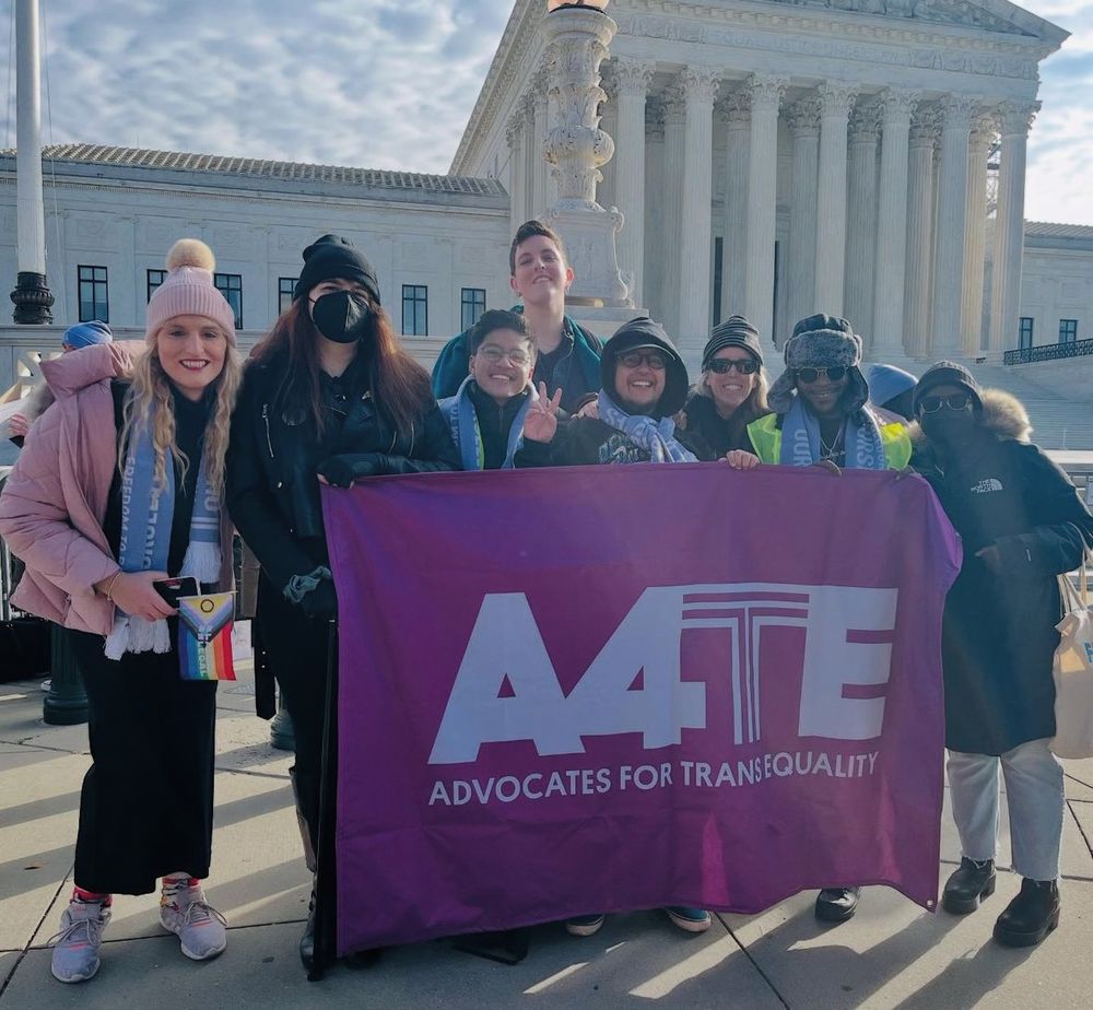 Eight people pose in a group in front of the US Supreme Court. They are holding a banner with the logo of Advocates for Trans Equality.