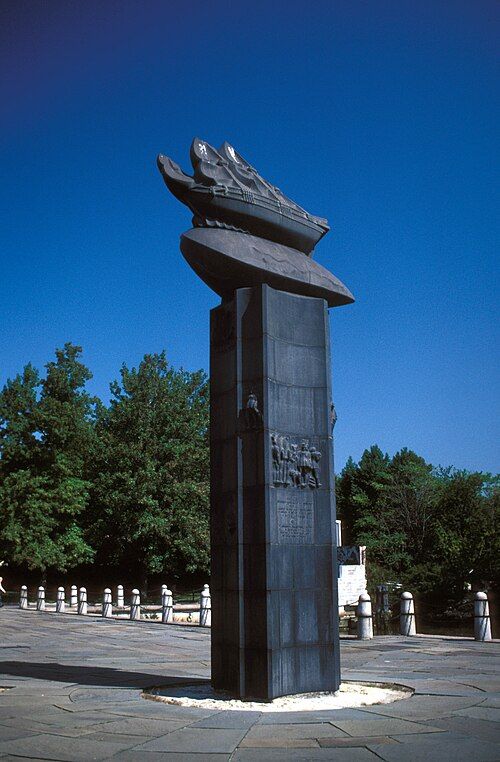 A steel column surmounted by sculpture of boat on a wave, with bas relief of settlers.

Wikipedia caption: "Monument erected at the site of the first landing on the banks of the Christina River designed by Swedish sculptor Carl Milles" 