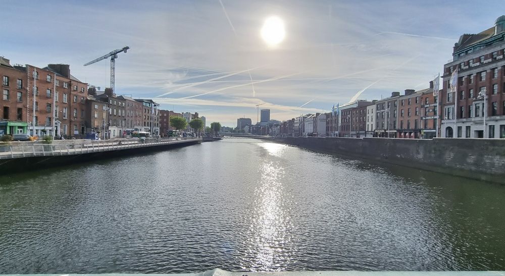 Morning sun over the River Liffey in Dublin, viewed from a bridge, with light reflecting off the water. 